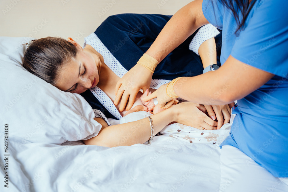 Mixed races woman lying on bed and breastfeeding her infant new born baby at hospital room. Female breastfeeding consultant helping mom breast feeding her child. Baby eating mother's milk. Mixed races woman lying on bed and breastfeeding her infant new born baby at hospital room. Female breastfeeding consultant helping mom breast feeding her child. Baby eating mother's milk.