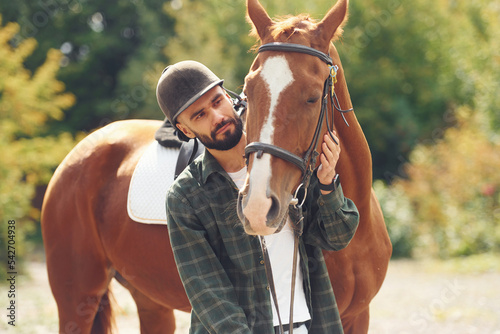 In protective hat. Young man with a horse is outdoors