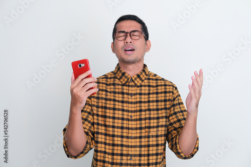 Adult Asian man showing disappointment while holding mobile phone