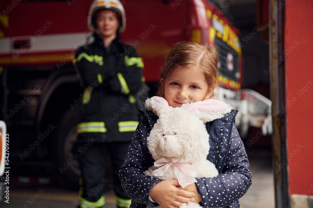 Kid is holding bunny toy. Firefighter woman in uniform is with a little girl Kid is holding bunny toy. Firefighter woman in uniform is with a little girl