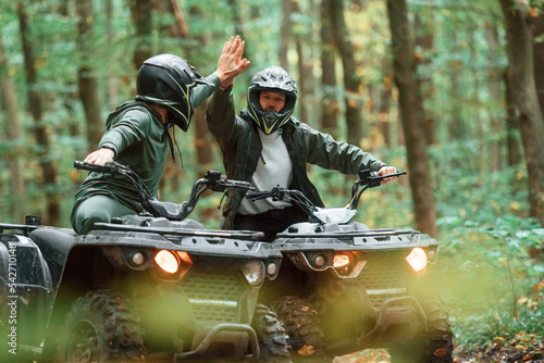 Giving high fives by the hands. Two male atv riders is in the forest together