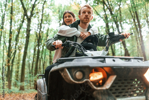 Man is handling the transport. Young couple riding a quad bike in the forest