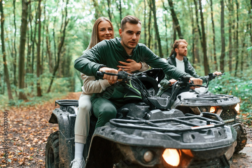 Riding and smiling. Young couple riding a quad bike in the forest