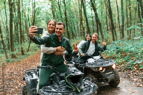 Making a selfie by smartphone. Two couples on a quad bike in the forest during the day