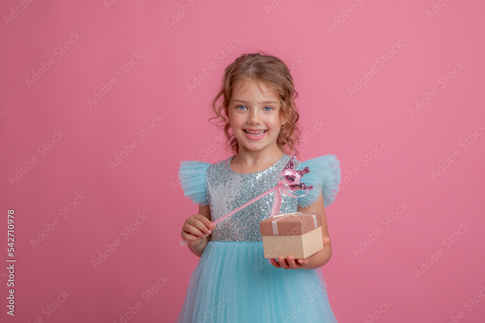 a cute little girl in a beautiful dress holds a fairy's magic wand and a gift on a pink background