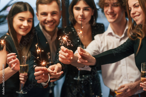 With new year sparklers. Group of people in beautiful elegant clothes are indoors together