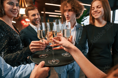 Taking glasses with champagne. Group of people in beautiful elegant clothes are celebrating New Year indoors together