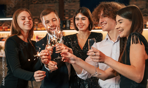 Amazing sparklers. Group of people in beautiful elegant clothes are celebrating New Year indoors together