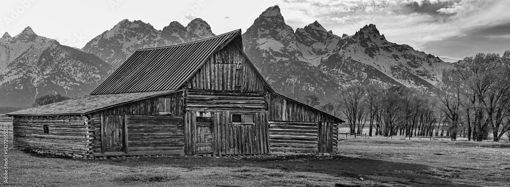 Φωτογραφία Grayscale shot of a old wooden house with snow capped mountains