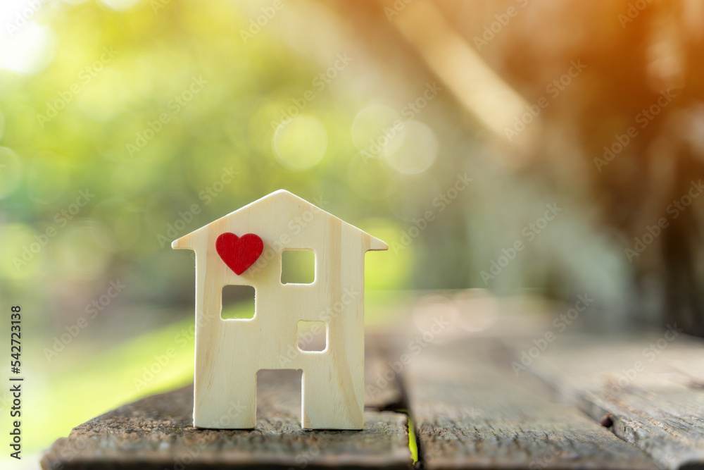 Wooden house model and red heart put on the wood on sunlight in the public park, The buying a new real estate as a gift to family or the one loved concept. Wooden house model and red heart put on the wood on sunlight in the public park, The buying a new real estate as a gift to family or the one loved concept.
