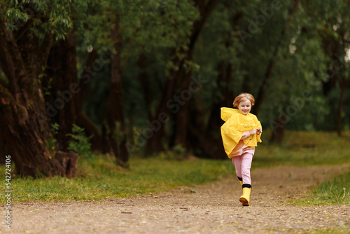  Happy funny baby under autumn shower. Girl running merrily laughing in the rain