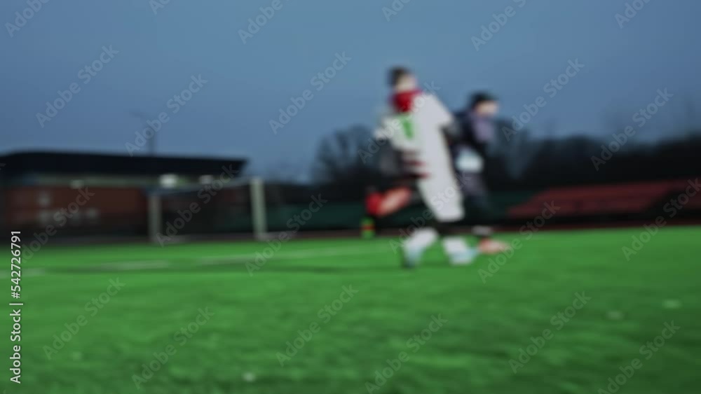 Soccer game in the evening in small stadium. Blurred. Football players give passes among themselves near centre circle. Teams in uniform, warm clothes, hats, thermal underwear are playing match Soccer game in the evening in small stadium. Blurred. Football players give passes among themselves near centre circle. Teams in uniform, warm clothes, hats, thermal underwear are playing match