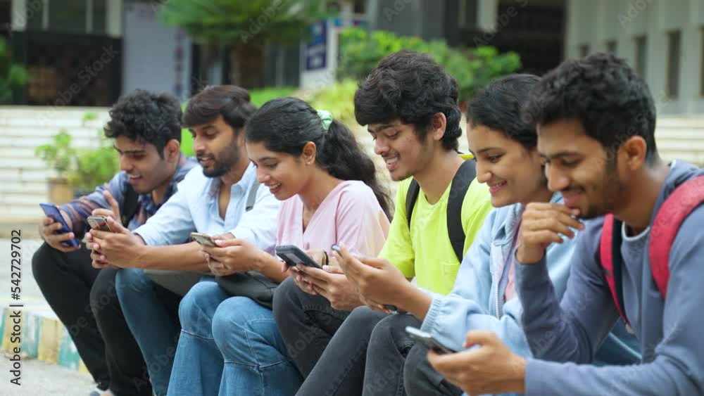 Group of indian college students busy using mobile phone at campus during leisure - concept of social media sharing, education and internet addiction. Group of indian college students busy using mobile phone at campus during leisure - concept of social media sharing, education and internet addiction.