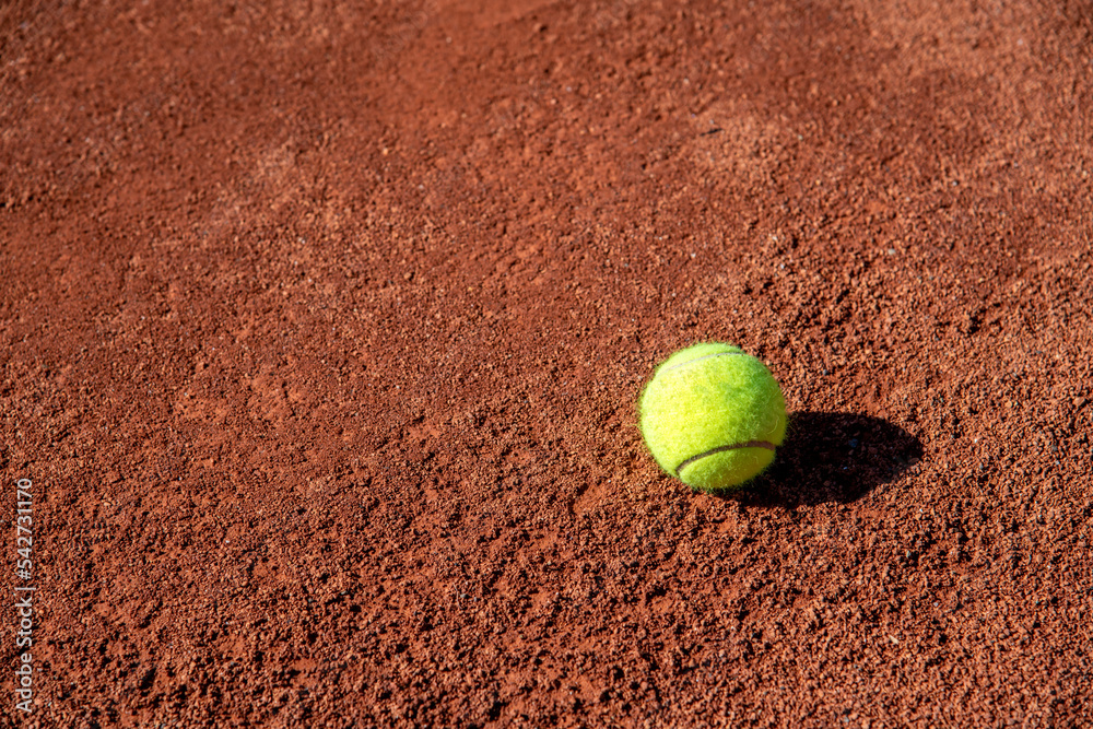 Tennis ball standing on clay tennis court on a sunny day