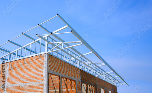 Perspective side view of brick wall and shed roof framing structure of row houses in under construction against blue sky background