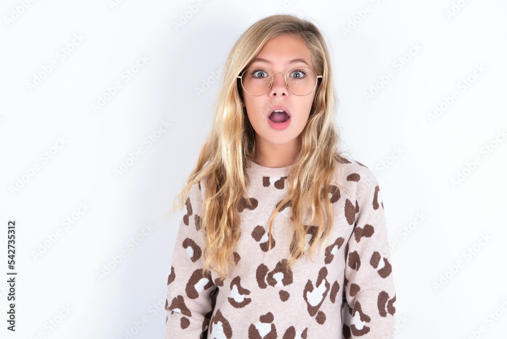little caucasian kid girl wearing animal print sweater over white background having stunned and shocked look, with mouth open and jaw dropped exclaiming: Wow, I can't believe this. Surprise and shock