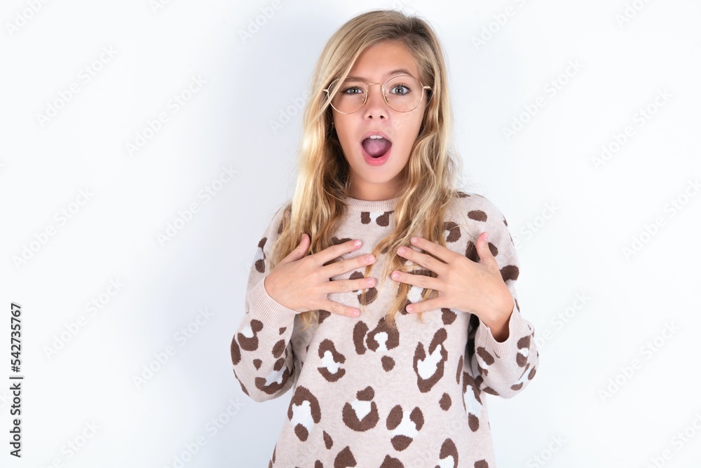 little caucasian kid girl wearing animal print sweater over white background keeps hands on chest feeling shocked and scared, mouth widely opened, stares at camera saying: Who, me? little caucasian kid girl wearing animal print sweater over white background keeps hands on chest feeling shocked and scared, mouth widely opened, stares at camera saying: Who, me?