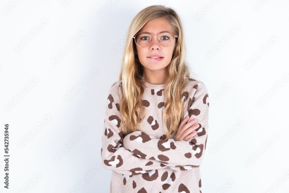 little caucasian kid girl wearing animal print sweater over white background bitting his mouth and looking worried and scared crossing arms, worry and doubt. little caucasian kid girl wearing animal print sweater over white background bitting his mouth and looking worried and scared crossing arms, worry and doubt.