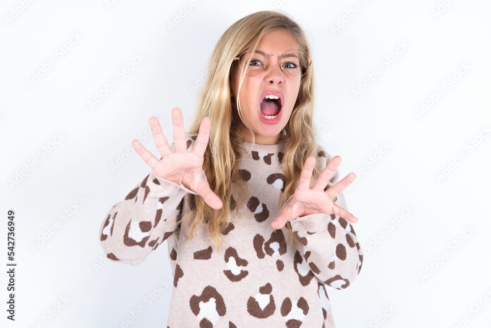 Dissatisfied little caucasian kid girl wearing animal print sweater over white background frowns face, has disgusting expression, shows tongue, expresses non compliance, irritated with somebody. Dissatisfied little caucasian kid girl wearing animal print sweater over white background frowns face, has disgusting expression, shows tongue, expresses non compliance, irritated with somebody.
