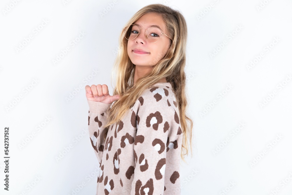 Closeup of cheerful beautiful caucasian teen girl wearing animal print sweater over white wall looks joyful, satisfied and confident, points at himself with thumb. Closeup of cheerful beautiful caucasian teen girl wearing animal print sweater over white wall looks joyful, satisfied and confident, points at himself with thumb.