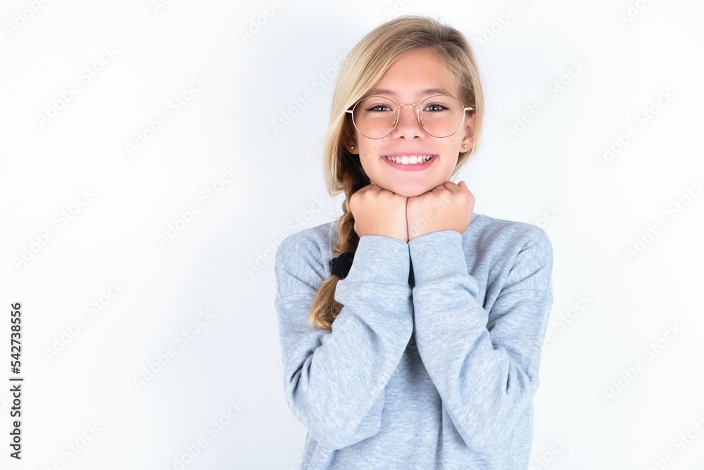 Satisfied beautiful caucasian teen girl wearing gray sweater over white wall touches chin with both hands, smiles pleasantly, rejoices good day with lover Satisfied beautiful caucasian teen girl wearing gray sweater over white wall touches chin with both hands, smiles pleasantly, rejoices good day with lover