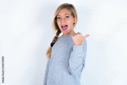 Impressed beautiful caucasian teen girl wearing gray sweater over white wall point back empty space
