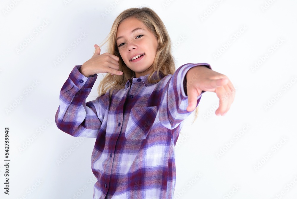 beautiful caucasian teen girl wearing plaid purple shirt over white wall smiling cheerfully and pointing to camera while making a call you later gesture, talking on phone beautiful caucasian teen girl wearing plaid purple shirt over white wall smiling cheerfully and pointing to camera while making a call you later gesture, talking on phone