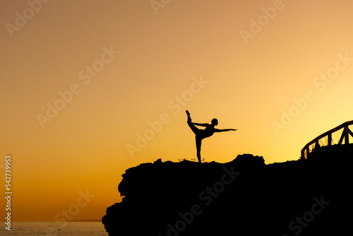 Woman doing yoga under a beautiful sunset in the coast. Flexible person silhouette doing exercise in the exterior.  photo