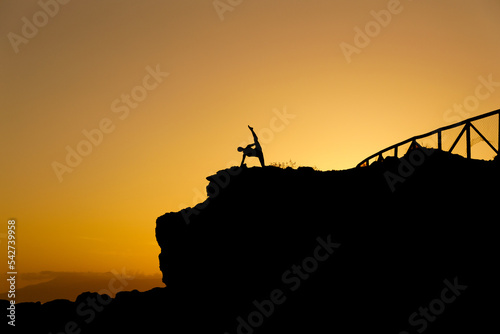 Woman doing yoga under a beautiful sunset in the coast. Woman silhouette doing exercise. Flexible person silhouette doing exercise in the exterior. Zen freedom