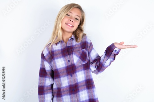 beautiful caucasian teen girl wearing plaid purple shirt over white wall smiling cheerful presenting and pointing with palm of hand looking at the camera.