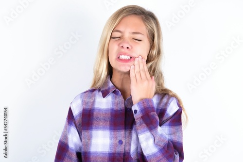 beautiful caucasian teen girl wearing plaid purple shirt over white wall touching mouth with hand with painful expression because of toothache or dental illness on teeth.