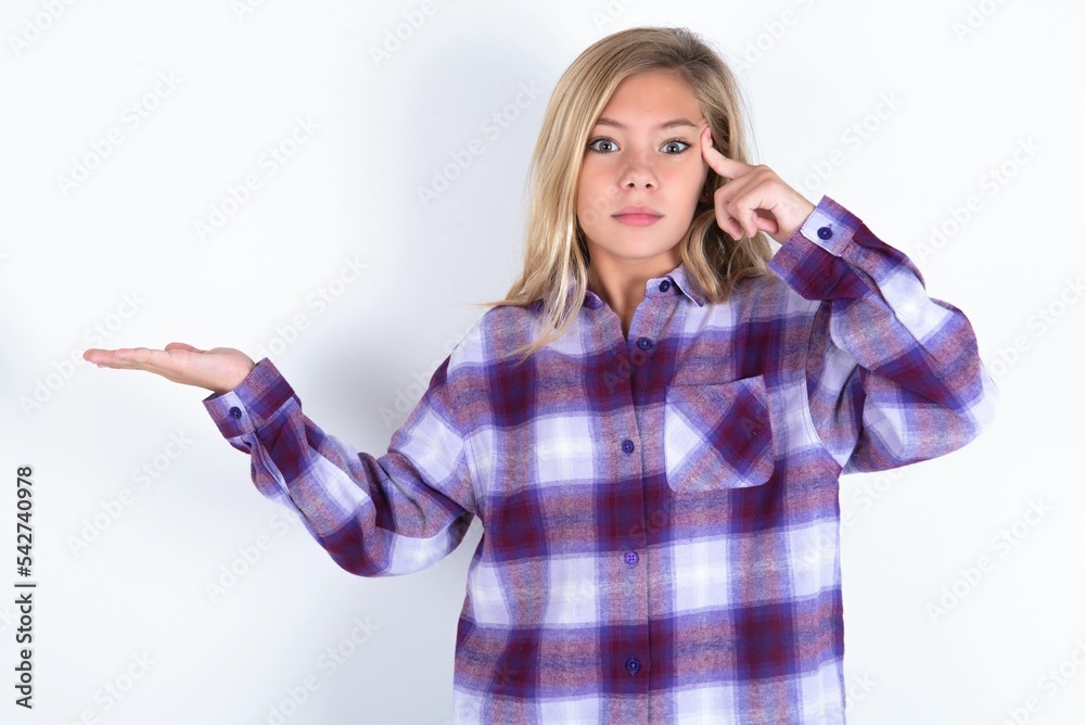 Obraz premium beautiful caucasian teen girl wearing plaid purple shirt over white wall confused and annoyed with open palm showing copy space and pointing finger to forehead. Think about it.