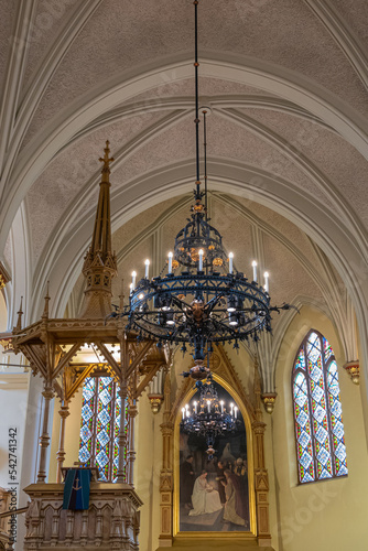 Finland, Kotka - July 18, 2022: Kotka-Kymin Parish Church or Seurakuntayhtymä. Artful and elaborate hanging light fixture with pulpit and painting in back against yellow walls and white cerch, Finland photo