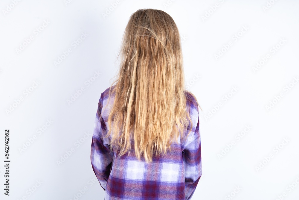 The back view of a beautiful caucasian teen girl wearing plaid purple shirt over white wall. Studio Shoot. The back view of a beautiful caucasian teen girl wearing plaid purple shirt over white wall. Studio Shoot.