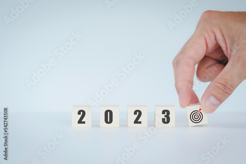 Hand putting wooden cube goal target New Year 2023 concept, mobile stick with new year 2023, business vision and horizontal size image.
