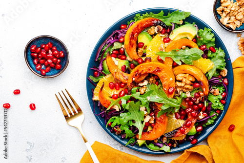 Fresh autumn pumpkin salad with baked pumpkin slices, red cabbage, avocado, arugula, pomegranate seeds and walnuts. Healthy vegan, vegetarian eating, comfort food. White background. Top view photo