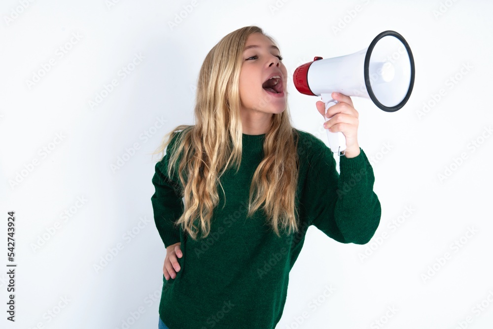 Funny beautiful caucasian teen girl wearing green knitted sweater over white wall People sincere emotions lifestyle concept. Mock up copy space. Screaming in megaphone. Funny beautiful caucasian teen girl wearing green knitted sweater over white wall People sincere emotions lifestyle concept. Mock up copy space. Screaming in megaphone.