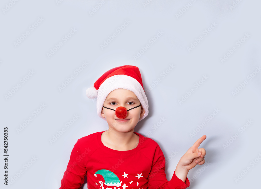 Cute caucasian kid boy in red Santa's hat and red nose points with his finger on empty copy space for design or text. Banner. Christmas mockup template for card or certificate.