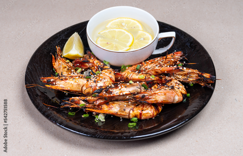 Close-up with a delicious snack. Grilled shrimp on beautiful black plate. Water and lemon.