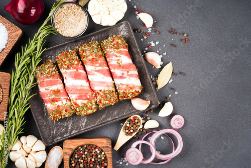 Traditional Balkan food cevapcici or Romanian mititei ready for grilling or bbq. Raw minced meat rolls wrapped with bacon and seasonings in container over dark concrete background photo