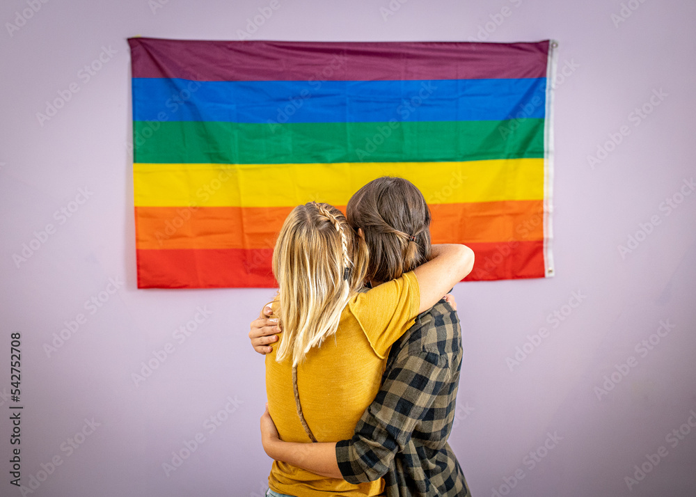 Beautiful lesbian couple with rainbow flag on the wall of their new ...