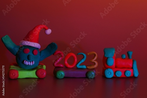 A toy train with the number 2023 and a coronavirus figurine. Festive event  Christmas and New Year. A symbol of the advent of holidays. Bright colored background.