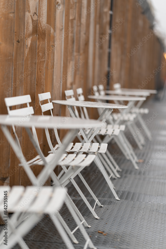 White chairs and tables after a rainy day on a brown wall background. - obrazy, fototapety, plakaty 