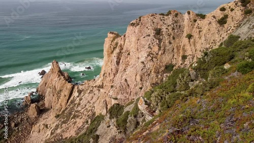 Cold water of the ocean washes against the rugged coastline full of cliffs, 4k aerial view.