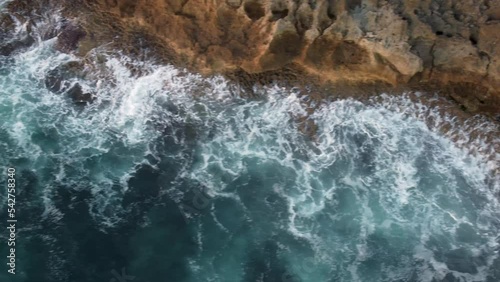 Beautiful Aerial top view 4k footage by drone of ocean blue waves break on high cliff of a rocky mountain.