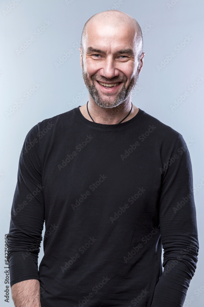 Laughing bald man in a black shirt. Brutal charismatic adult guy. Grey background. Vertical. Laughing bald man in a black shirt. Brutal charismatic adult guy. Grey background. Vertical.