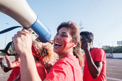 Middle-aged woman cheering her team with the megaphone outdoors
