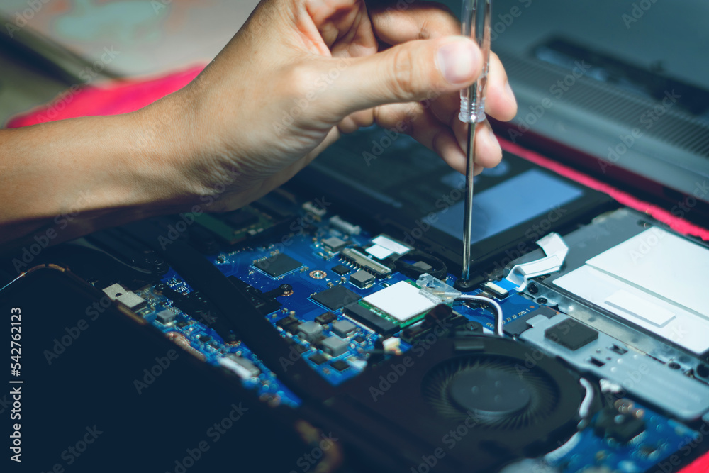 The hand is using a screwdriver to tighten the nut. To change the battery of a notebook computer by yourself. Changing electronic devices by yourself concept. The hand is using a screwdriver to tighten the nut. To change the battery of a notebook computer by yourself. Changing electronic devices by yourself concept.