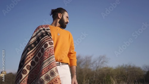 Slow-motion shot of a standing male with beard manbun eyeglasss orange blouse necklace with pendant photo