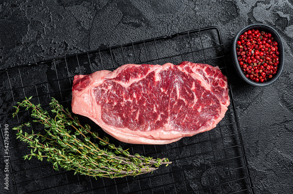 Raw striploin or New York  beef meat steak ready for BBQ. Black background. Top view